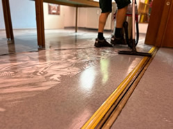 Ein Mitarbeiter der Herdegen Gebäudeservice GmbH saugt mit einem Wassersauger verschmutztes Reinigungswasser vom Boden bei einer Grundreinigung ab.