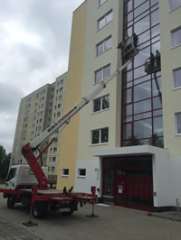 Mitarbeiter der Herdegen Gebäudeservice GmbH reinigen die Glasfassade eines mehrgeschossigen Wohngebäudes sicher aus einer Hubarbeitsbühne heraus. Der Reinigungseinsatz erfolgt in großer Höhe unter Einsatz professioneller Ausrüstung.