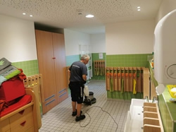 Ein Mitarbeiter der Herdegen Gebäudeservice GmbH führt eine maschinelle Grundreinigung des Bodens in einem Waschraum einer Kindertagesstätte durch.