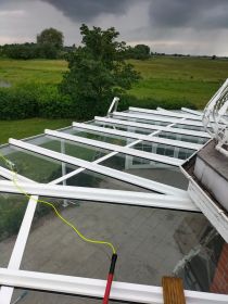 Ein Glasdach eines Wintergartens wird mit einer professionellen Reinigungsstange und Osmosetechnik gereinigt. Das Bild zeigt die effektive Entfernung von Schmutz und Belägen auf einem großflächigen Terrassendach mit weißem Rahmen.